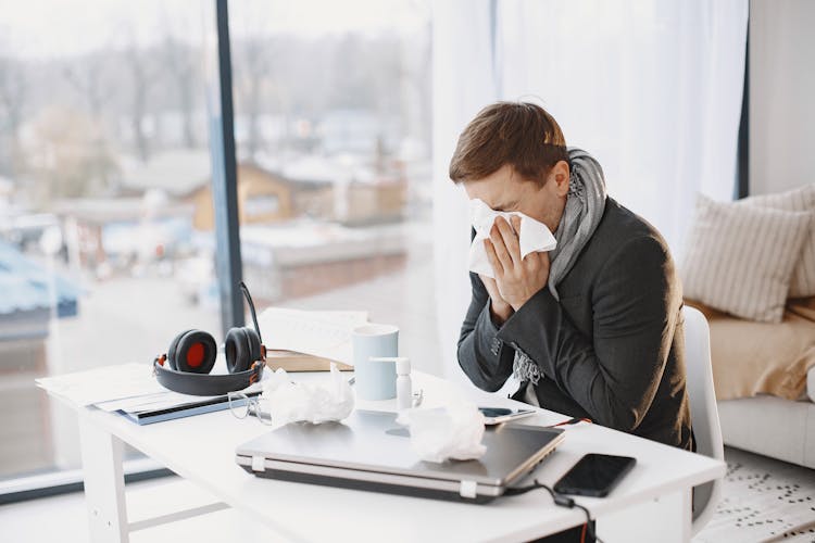 Ill Man Sitting At Desk And Sneezing 