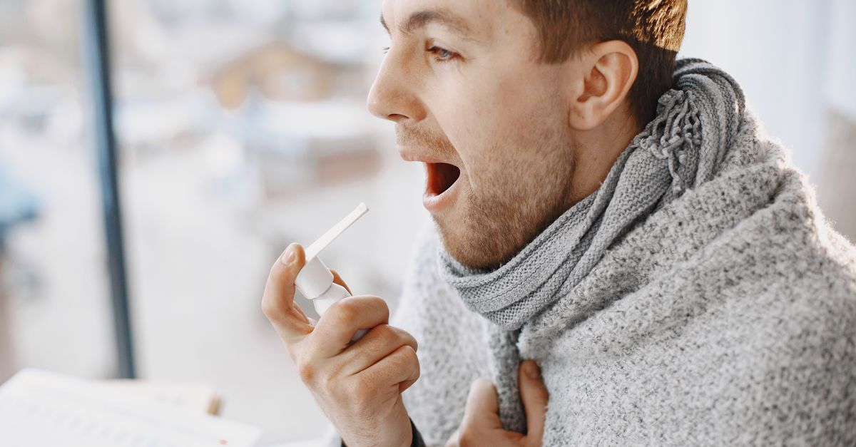An adult man uses a throat spray, wrapped in a blanket, appearing unwell indoors. - Evidence evidence guide for propolis respiratory symptoms meta-analysis