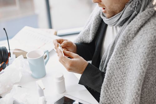 Free A man wrapped in a blanket, checking a thermometer while convalescing indoors. Stock Photo