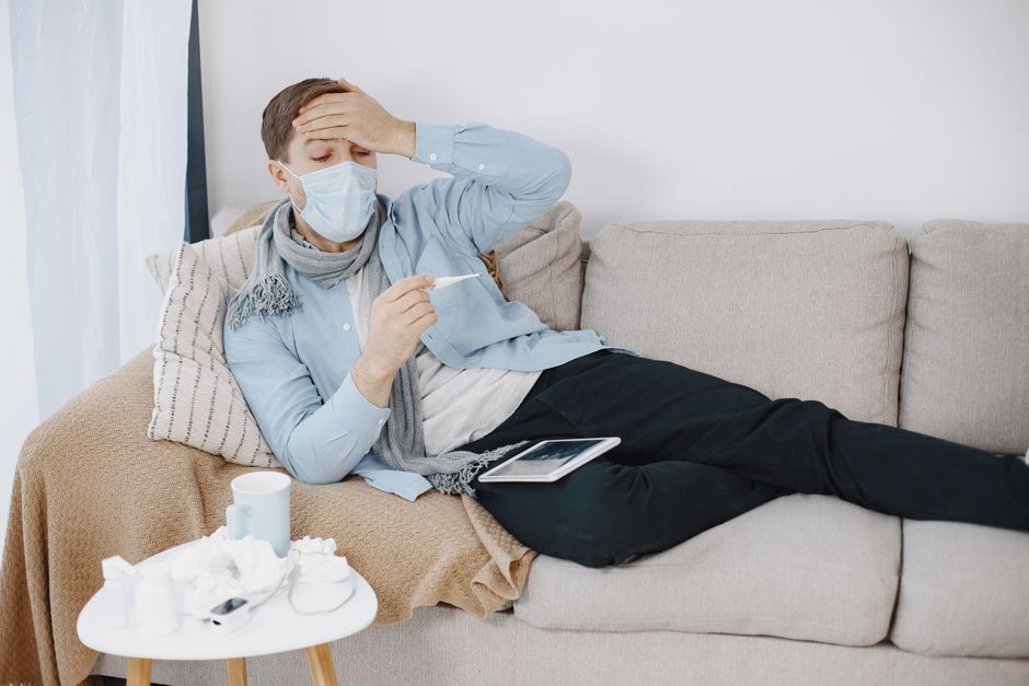 A man with a mask looks sick and checks his temperature at home.