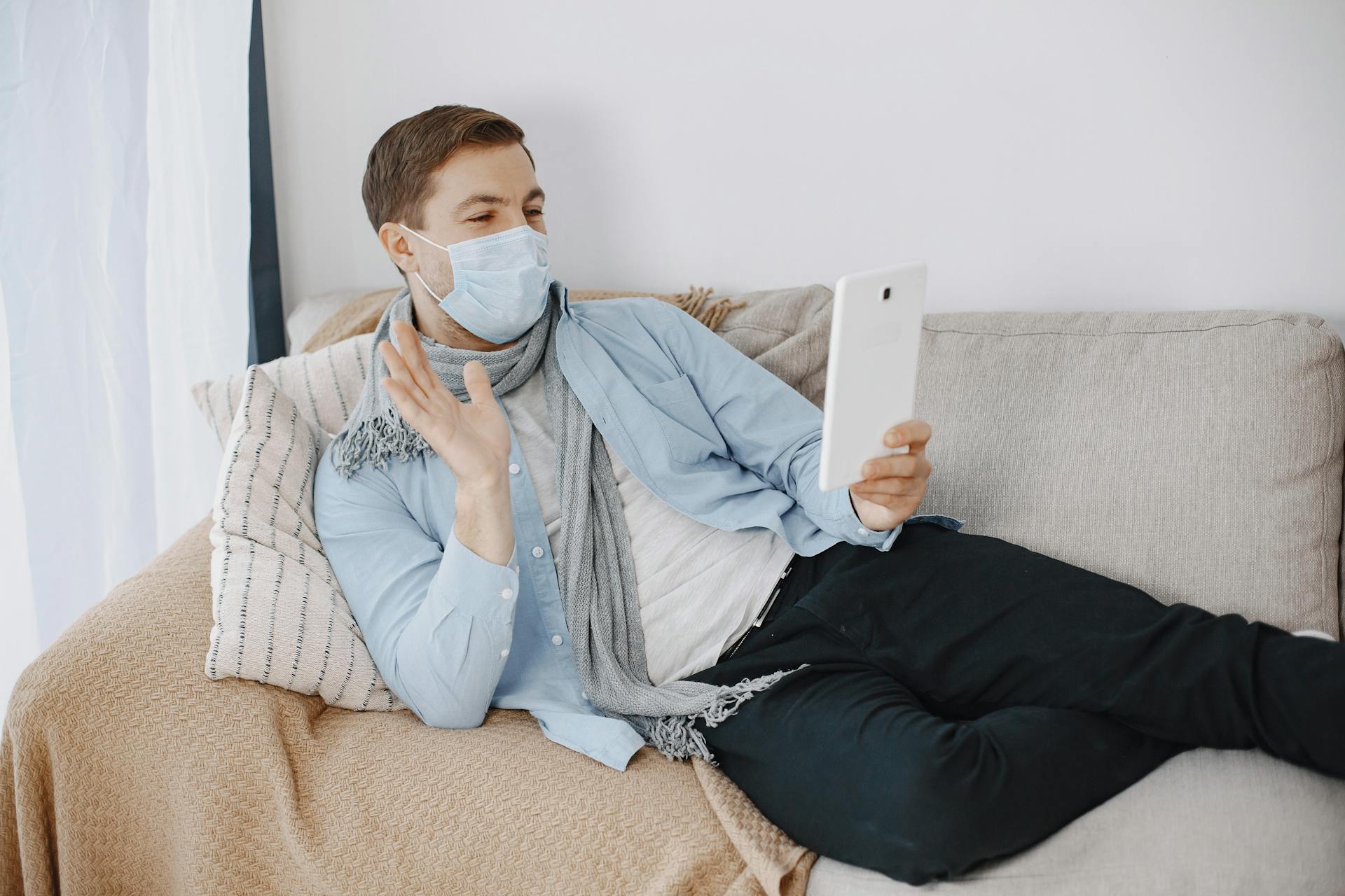 Young man wearing mask on video call at home, indicating a telemedicine consultation.