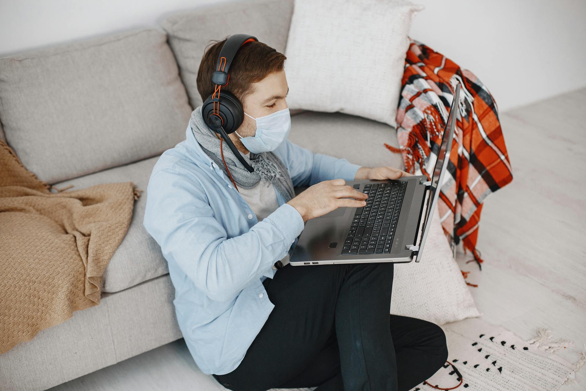 Man wearing mask using laptop for telehealth in a cozy home setting with headphones.