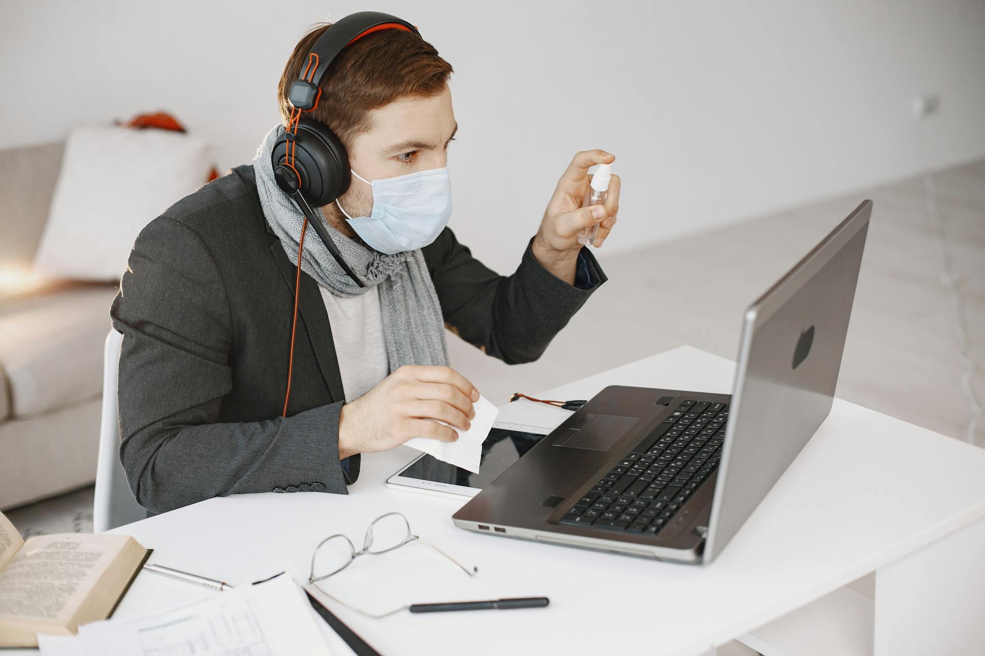 Person in a mask video calling using a laptop, focusing on telehealth from home.