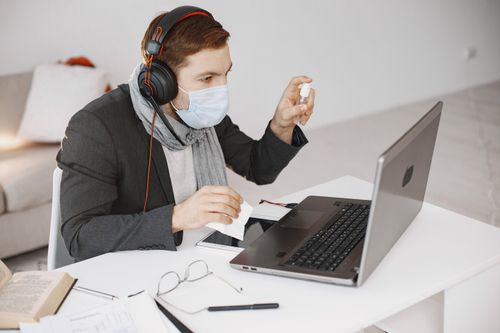 Free Person in a mask video calling using a laptop, focusing on telehealth from home. Stock Photo