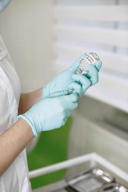 Free Close-up of a healthcare worker drawing a COVID-19 vaccine dose into a syringe, wearing gloves. Stock Photo