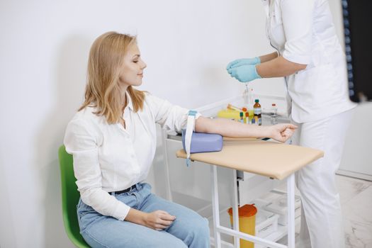 A woman sits in a clinic while a nurse prepares for a blood test procedure.