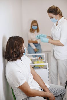 Medical professionals performing a blood test in a clinic setting with patients wearing facemasks.