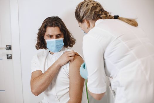 A healthcare worker wearing a mask gives a vaccine shot to a patient in a medical office.