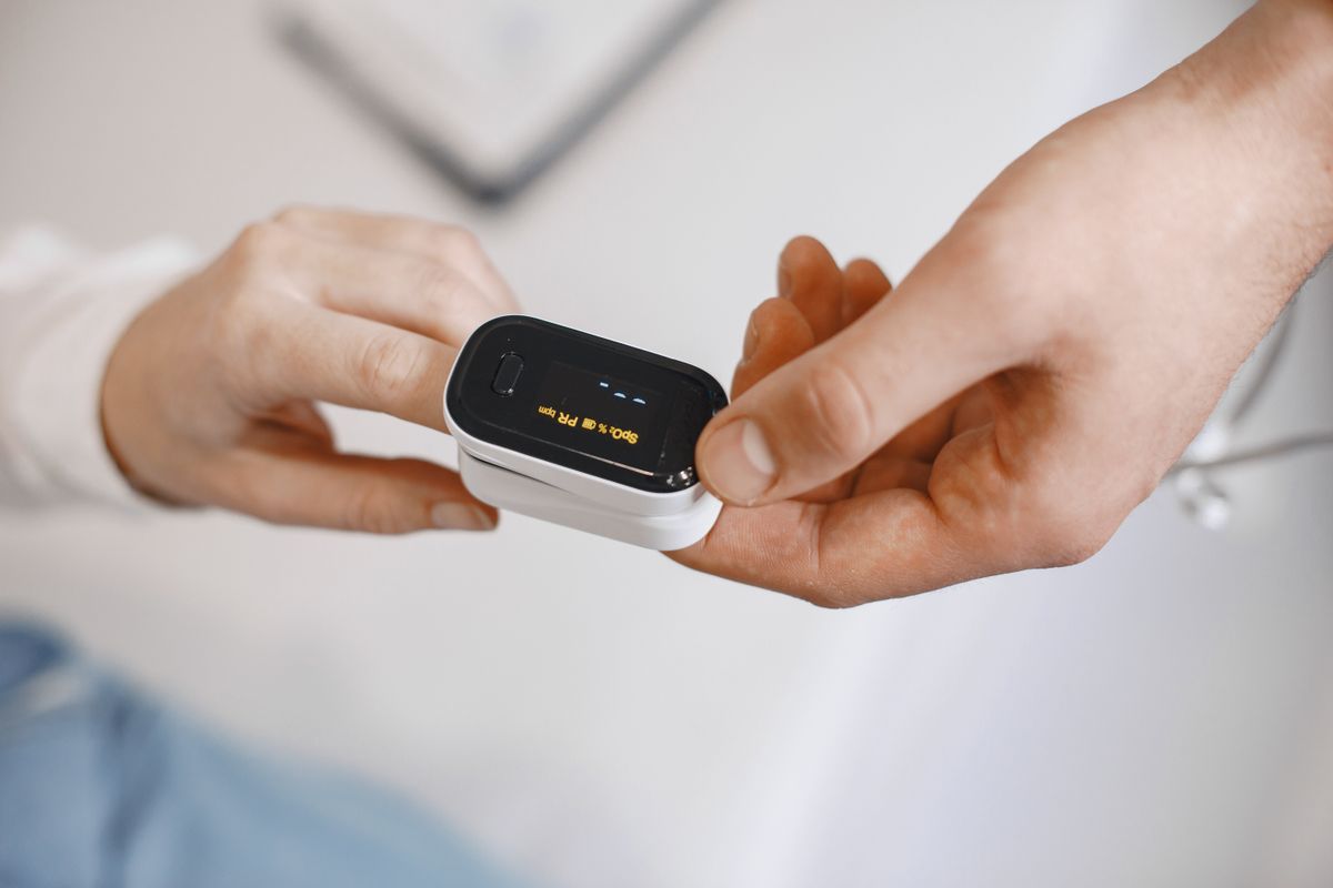 Fingertip oximeter in use, showing blood oxygen saturation and pulse rate