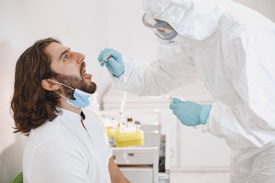 A Lab tech wearing PPE performs a mouth swab test on a man.  