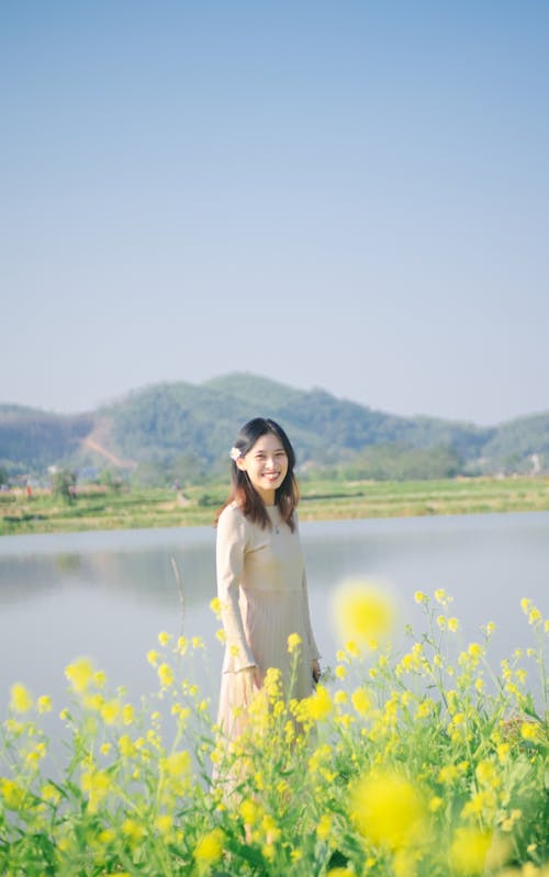 Smiling Woman in Beige Dress Standing near the Yellow Flowers
