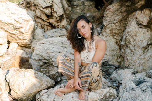 Free A Woman Wearing a Crochet Top and Floral Pants Sitting on a Rock Stock Photo