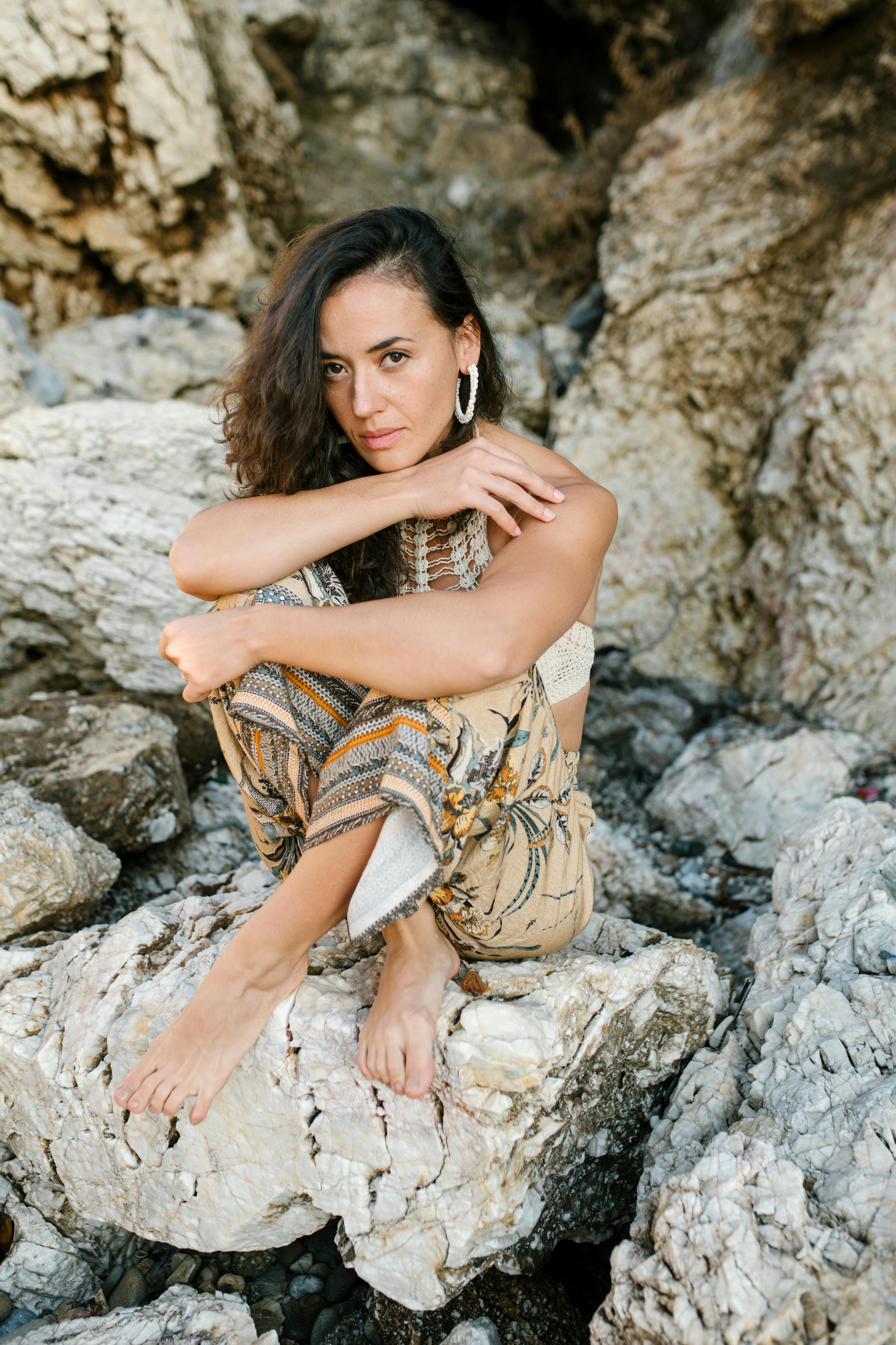 Woman in Brown and Black Sleeveless Dress Sitting on Gray Rock