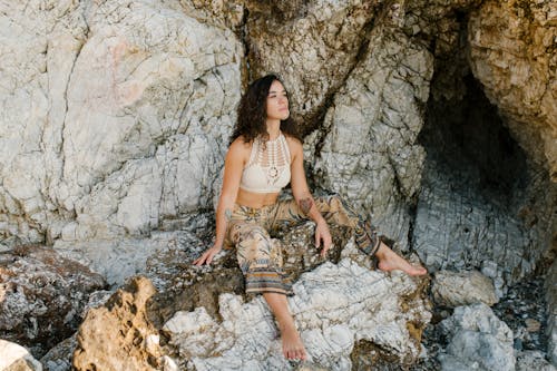 Young thoughtful female in summer clothes having rest outside rocky cave and looking away