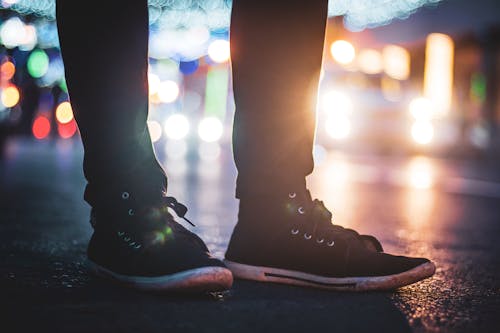 Crop unrecognizable male in casual outfi standing on paved road on blurred background of night city