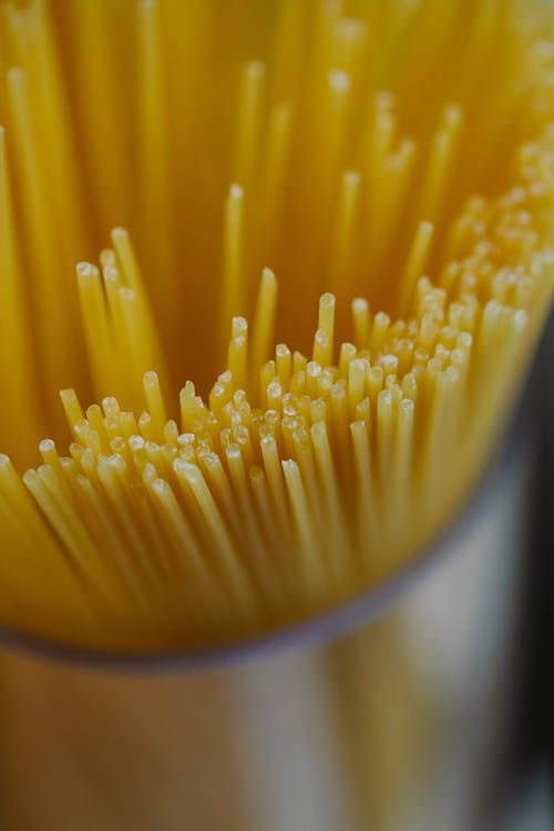 From above of uncooked bunch of spaghetti in glass bowl placed on surface on light kitchen