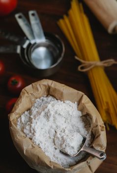 From above of uncooked bunch of spaghetti near metal dishware and bag with flour placed on wooden surface on light kitchen