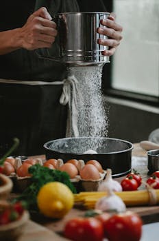Vibrant kitchen scene showcasing flour sifting over ingredients for a fresh homemade dish.