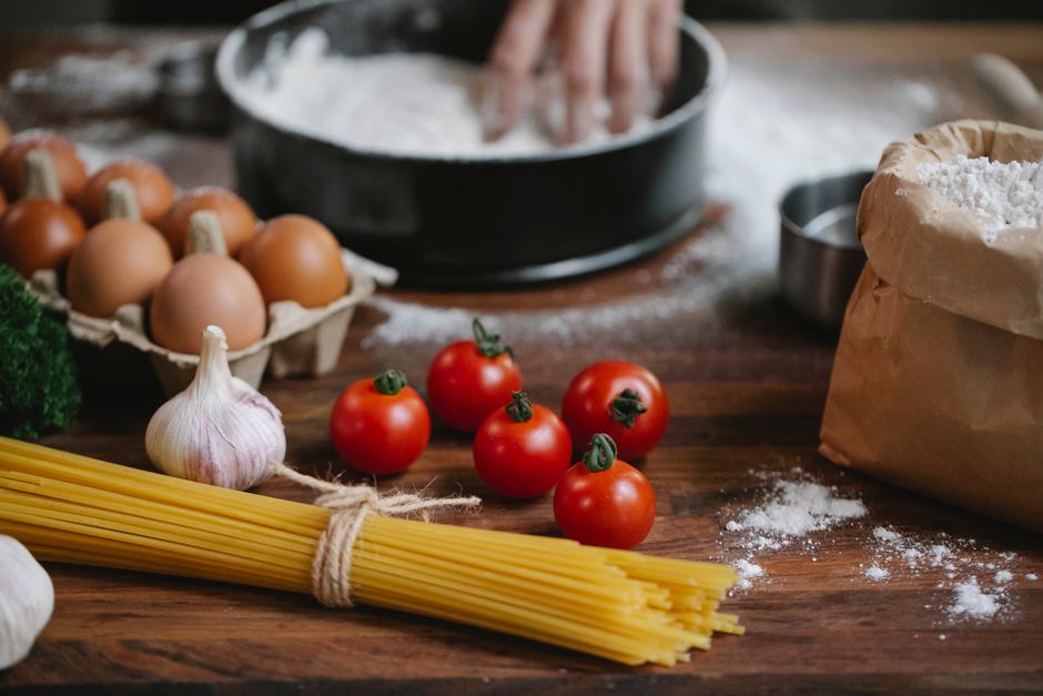 High angle of cherry tomatoes eggs garlic and spaghetti on table with crop chef kneading dough in baking dish