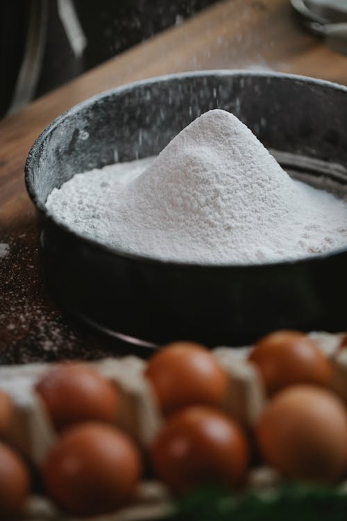 Free High angle of wheat flour pouring into baking dish placed on table with box of eggs Stock Photo