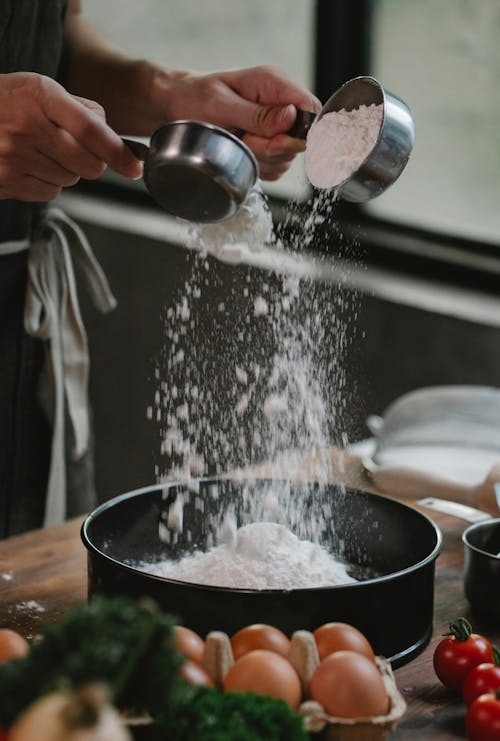 Free Crop anonymous chef pouring flour into baking dish while preparing ingredients for recipe with eggs and tomatoes Stock Photo