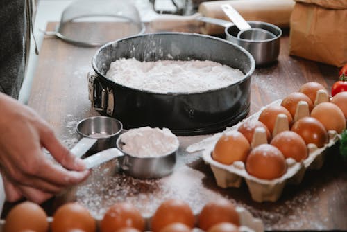 High angle of crop anonymous cook adding flour into baking dish while preparing pastry in kitchen