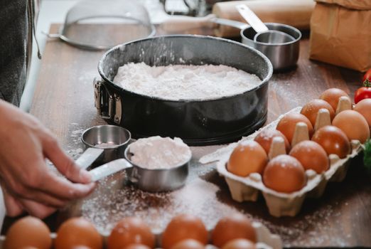 High angle of crop anonymous cook adding flour into baking dish while preparing pastry in kitchen