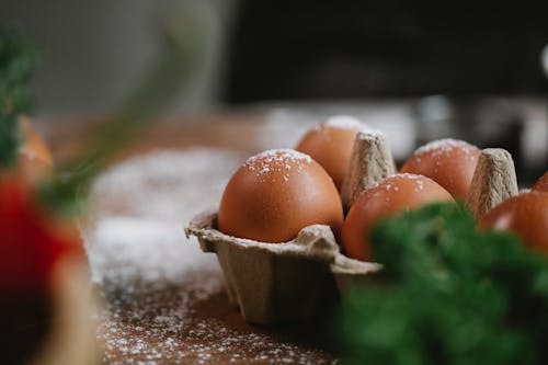 Free Uncooked chicken eggs in carton container with fresh greens placed on table with flour Stock Photo