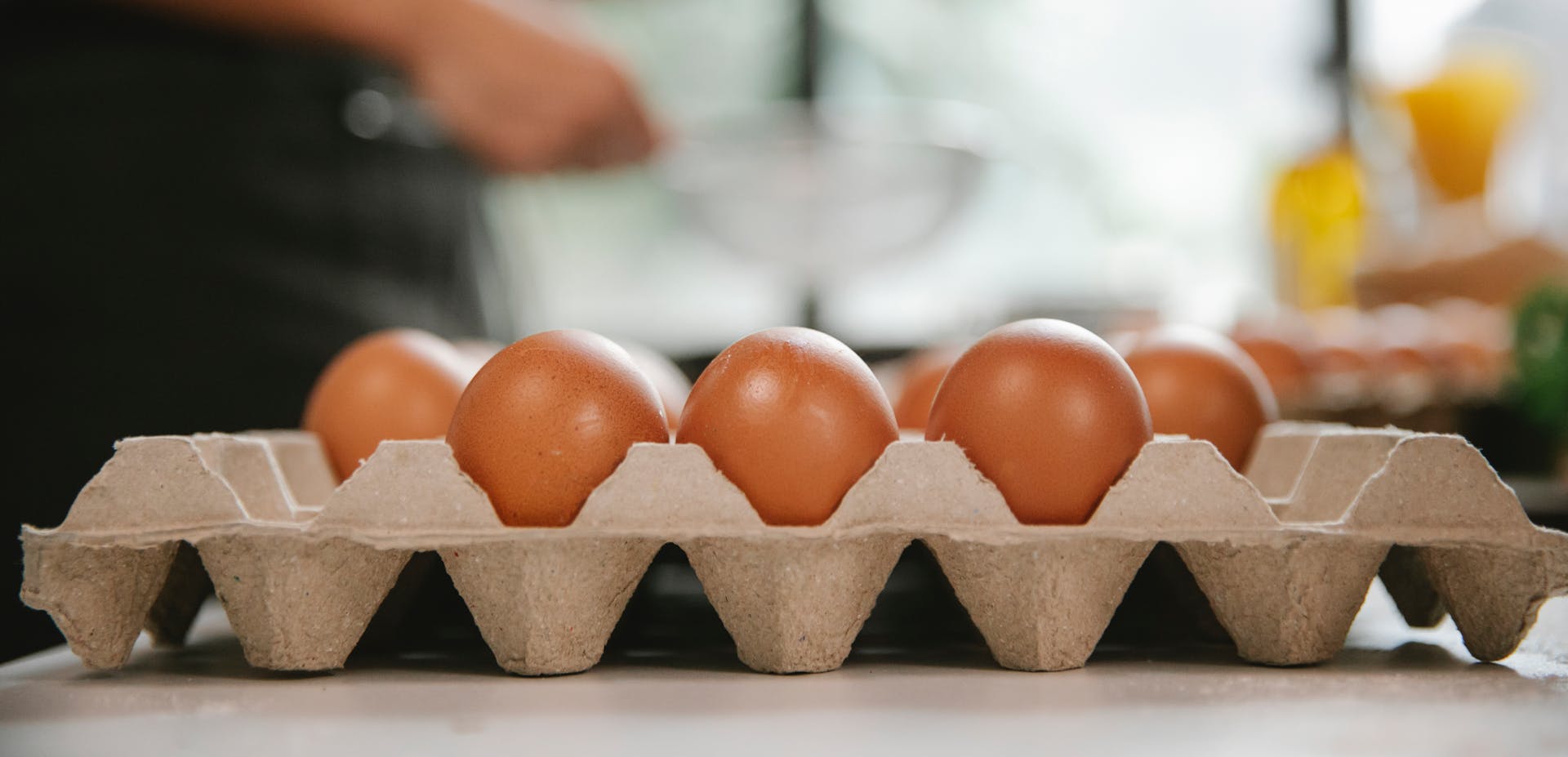 Eggs in carton container placed on table near chef cooking food in kitchen