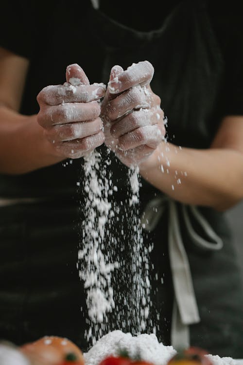 Crop anonymous cook in apron pouring flour while standing in kitchen and preparing meal