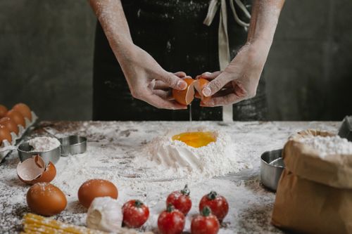 Free Crop anonymous chef preparing dough for recipe consisting of cherry tomatoes and spaghetti Stock Photo