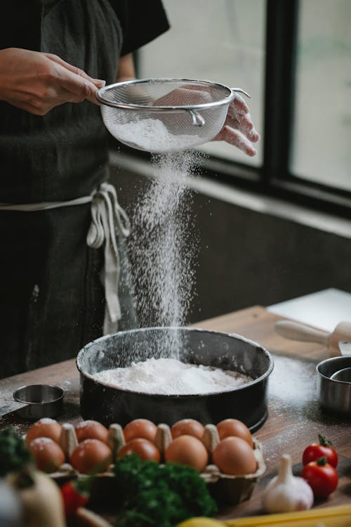 Chef sifting flour through sieve at kitchen