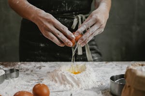 Person breaking egg to flour for pastry