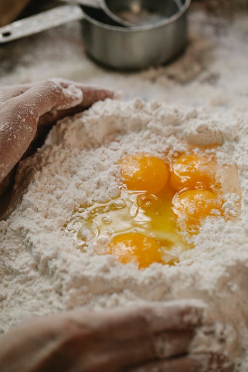 High angle of crop person kneading dough with flour and eggs while cooking at kitchen