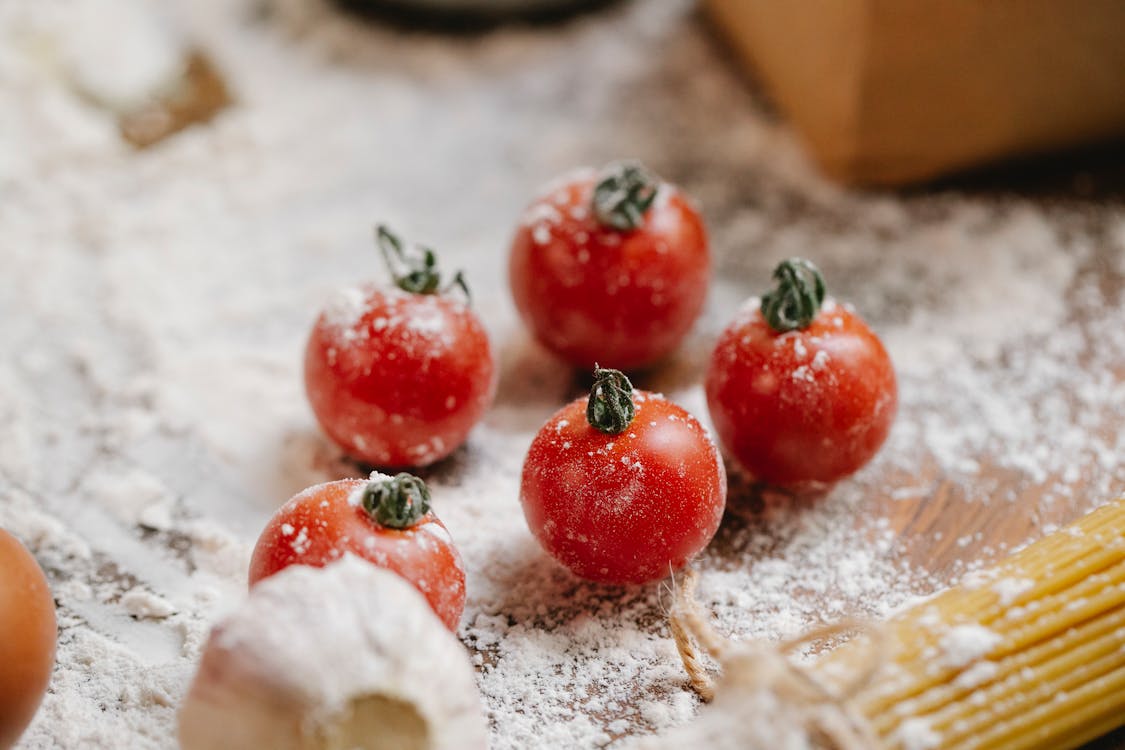 Free From above of ripe red cherry tomatoes with garlic and raw spaghetti on wooden table with flour Stock Photo