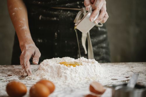 Free Crop anonymous cook pouring oil to flour and eggs while preparing pastry at home Stock Photo