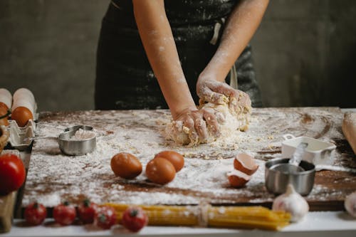 Crop chef kneading dough on wooden board