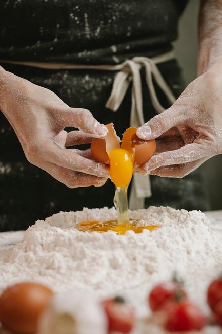 Fotomural Manos de chef rompiendo un huevo sobre la harina, preparando ingredientes culinarios en la cocina.