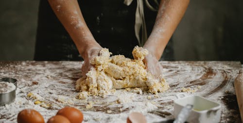 Unrecognizable person preparing dough while standing at table with eggs covered with flour in kitchen during cooking process at home