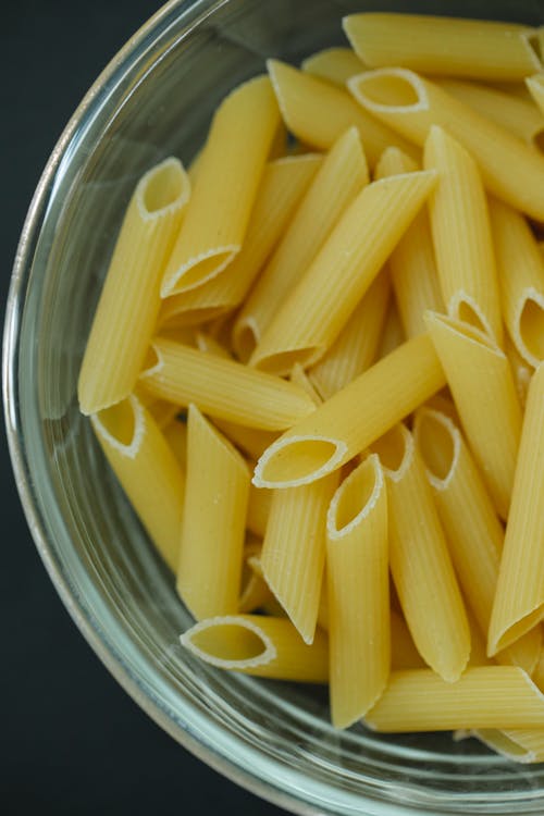 Free From above of traditional Italian dried uncooked penne pasta in glass bowl on table Stock Photo