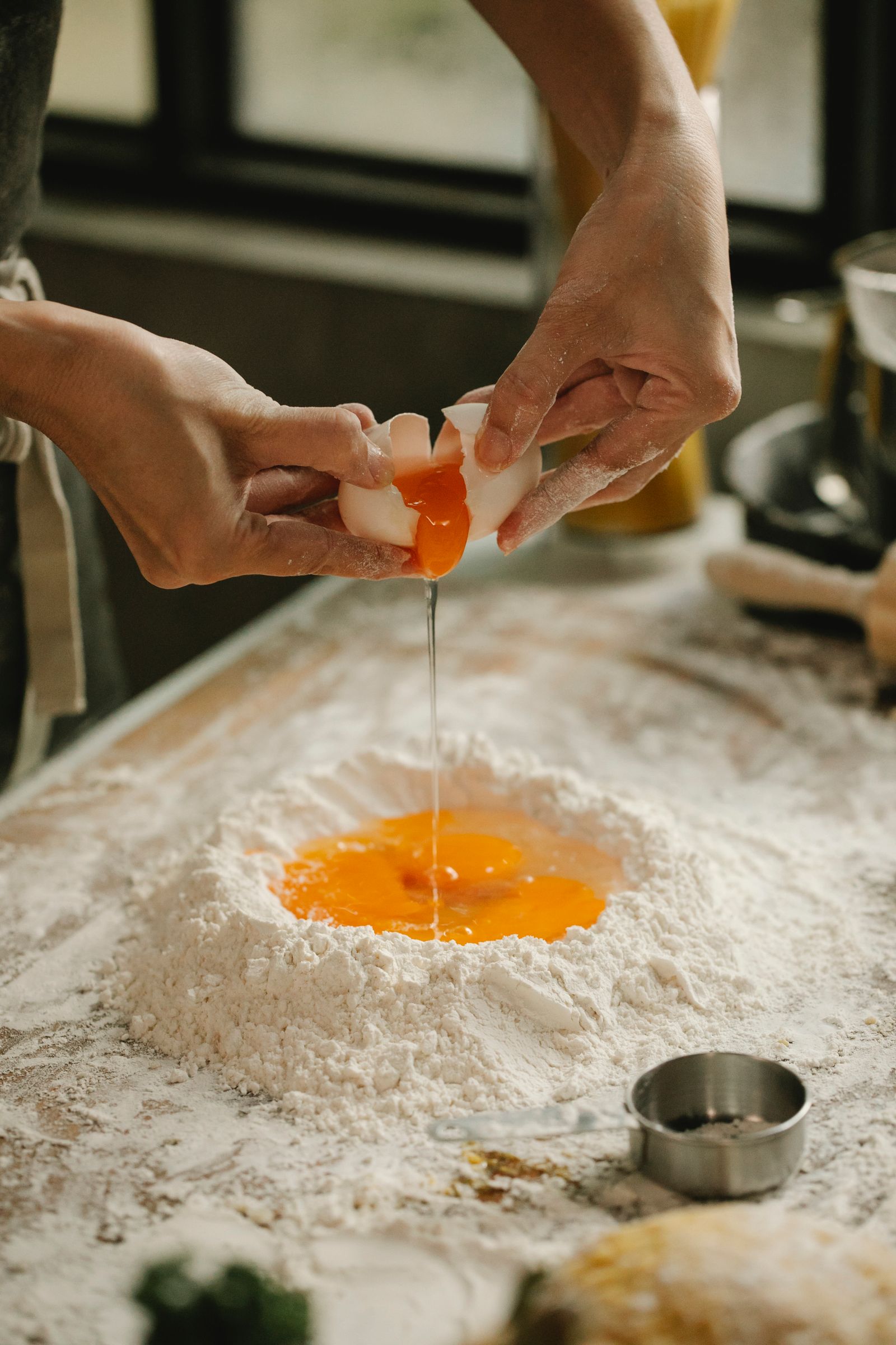 High angle of unrecognizable woman cracking egg into pile of flour making dough on table in kitchen