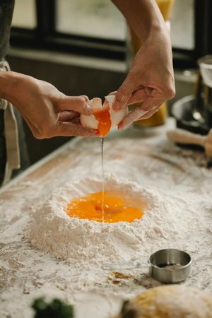 Overhead view of hands cracking an egg into flour to make dough — photo by Klaus Nielsen on Pexels