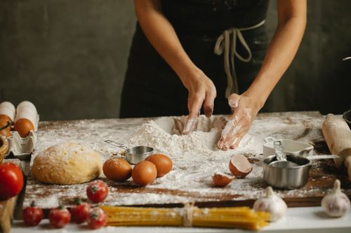 Free Unrecognizable woman in apron making dough with eggs and flour on chopping board on table with cooking ingredients on kitchen Stock Photo