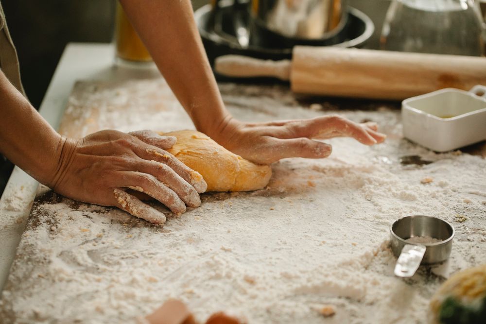 A baker's hands shaping soft dough on a flour-dusted board.