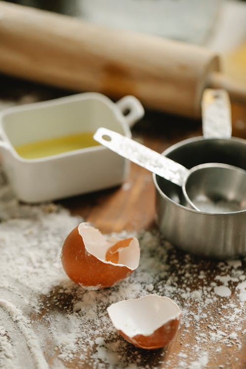 High angle of metal saucepans on wooden table with eggshells rolling pin and flour