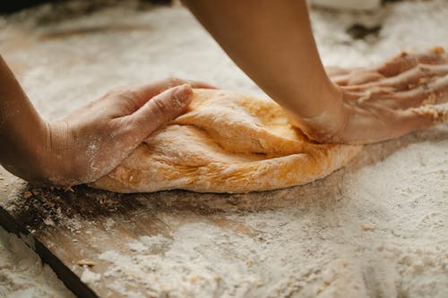 Unrecognizable female kneading soft fresh egg dough on cutting board with flour in kitchen