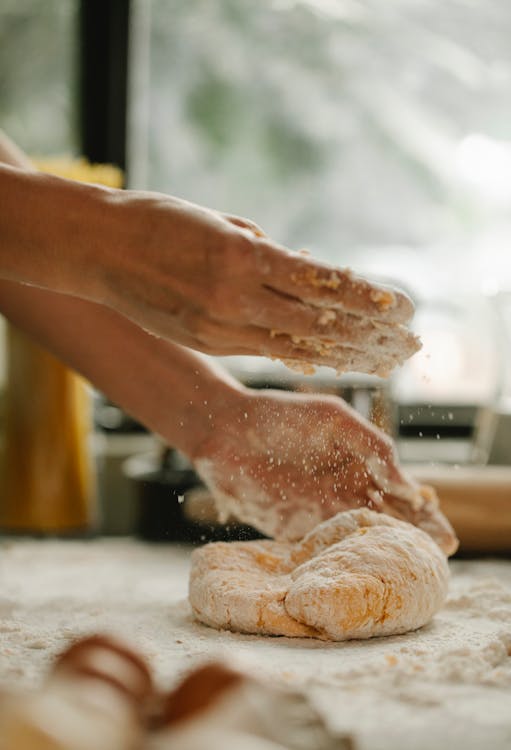 Unrecognizable woman kneading fresh and soft egg dough on table with flour in bakery