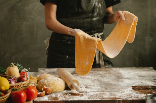 Free Crop anonymous female baker in black apron standing near table with rolled dough while cooking in kitchen Stock Photo