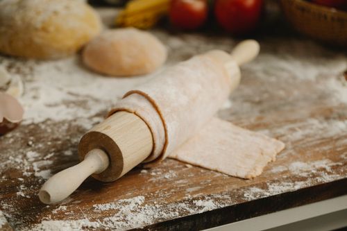 Free Wooden rolling pin with soft thin dough on table with spilled flour in kitchen Stock Photo