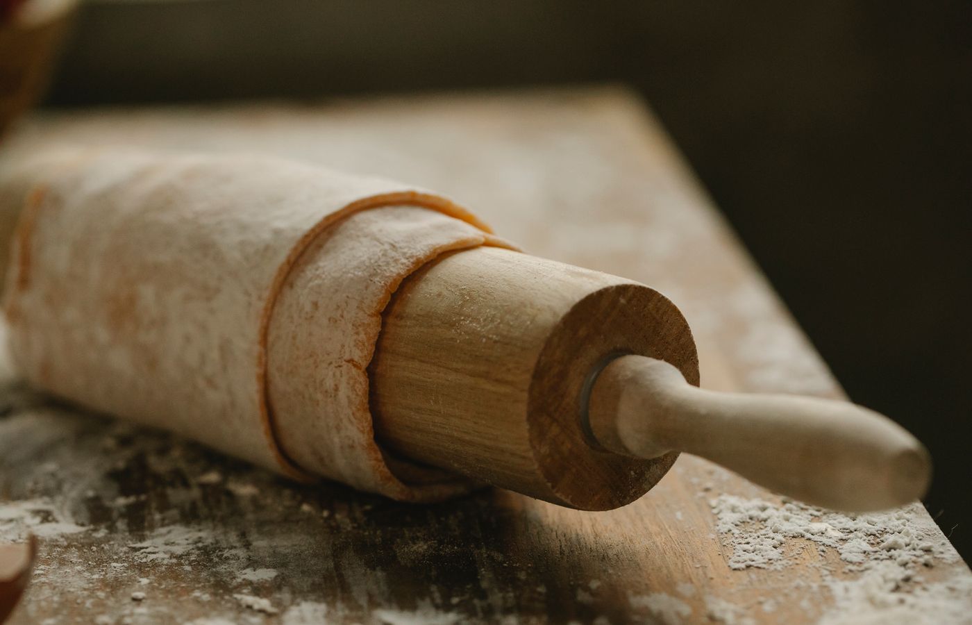 A rustic wooden rolling pin wrapped with dough on a flour-dusted table, creating a warm and homemade kitchen feel.